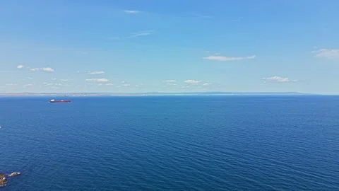 View of calm ocean with a cargo ship in distance under clear sky during daytime Stock Footage 345472969