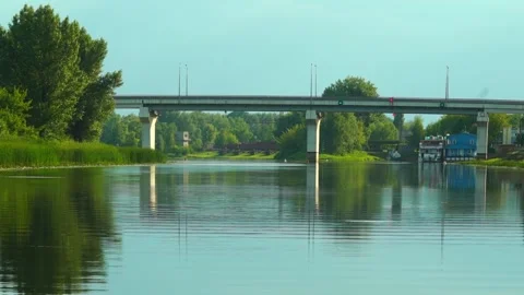 View of calm river with bridge and boats in the early evening light Видео 340447978