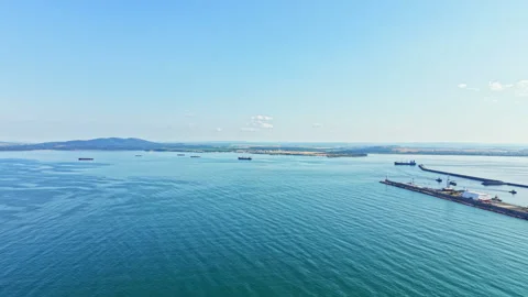View of a calm sea with distant ships and a port in the background on a clear 動画素材 341115467