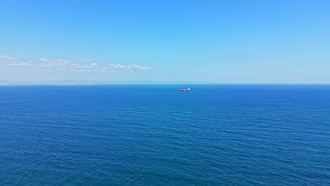 View of a calm sea with a ship sailing in the distance under a clear blue sky Stock Footage 344807209
