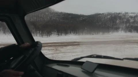 A view from the car to the snow-capped mountains covered with forest and a dirt 库存影片 153464198