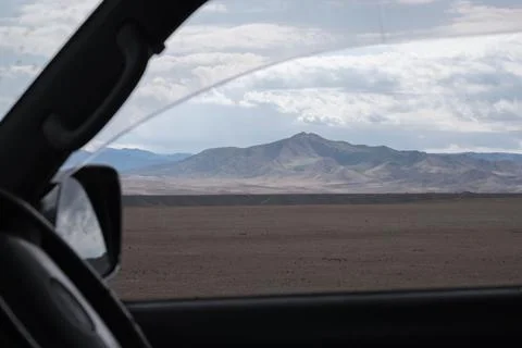 View from a car window of an arid desert landscape with mountains under a clo Stock Photos