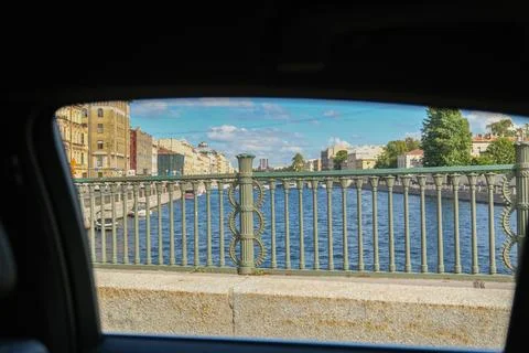 View from a car window of a bridge railing over a river with buildings and trees Stock Photos