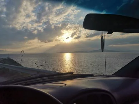View from the car window at sunset over the sea in a cloudy sky Stock Photos