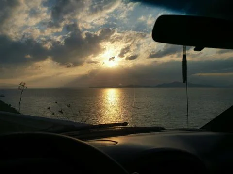 View from the car window at sunset over the sea in a cloudy sky Stock Photos