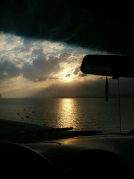 View from the car window at sunset over the sea in a cloudy sky Stock Photos