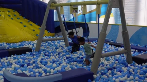 View of children playing on a swing in a playground filled with balls Stock Footage 275314931