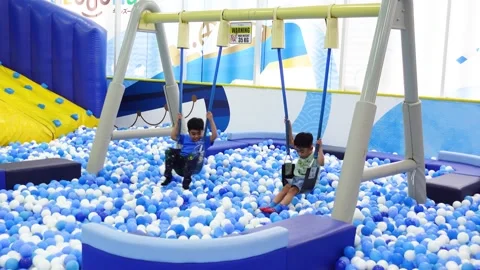 View of children playing on a swing in a playground filled with balls Stock Footage 275316952