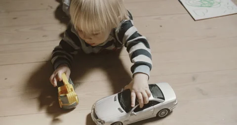 View of childs hands playing excavator near silver car model on the wooden floor Stock Footage 155397242