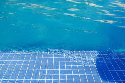 View of clear blue pool water over tiled edge with soft sunlight reflections. Stock Photos
