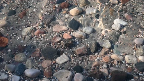 View into clear water on a beach with sand and multi-colored rounded stones. Stock Footage 139822456