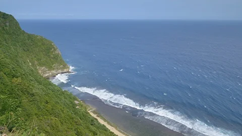 View from a cliff or hill on a beautiful beach with rock and dark blue water Stock Footage 114991444