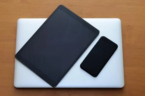 View on a closed laptop pc on a desk with a smartphone and tablet in a home o Stock Photos