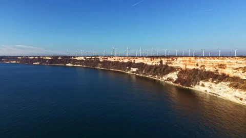 View of a coastal area with cliffs, wind turbines, and water under a clear blue Video stock 336636240