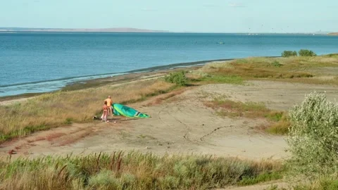 Up view of a couple on the beach. Man is fixing and setting sail for kiteboard. Stock Footage 139871018