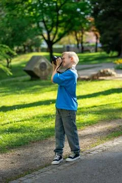 View of a cute boy in a blue t-shirt taking photos in the park for his blog Stock Photos