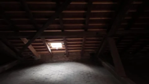 A view of dark attic space with a dormer window illuminating the space. An old Stock Footage 310753261