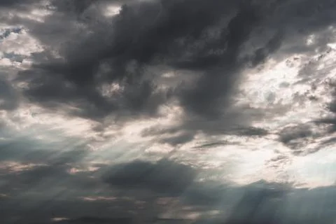 A view of a dark cumulus cloud in the sky through which the sun's rays break  Stock Photos