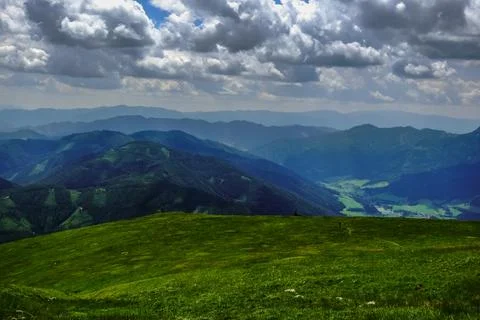 View to different shades of a mountain range while hiking on a green meadow Stock Photos