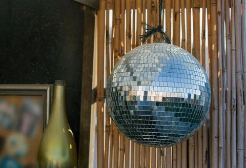 View of disco ball hanging in front of a bamboo backdrop, reflects light, cre Stock Photos