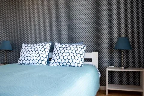 View of the double bed with a blue bedspread and white pillows against a dark Stock Photos
