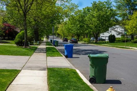 View down a residential tree lined street with green and blue trash bins  Foto stock