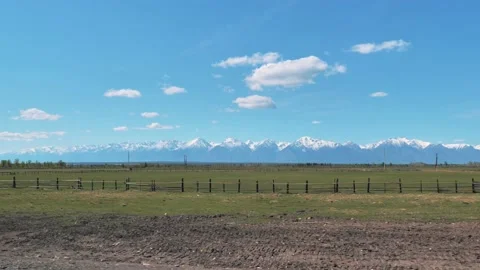 View from a driving car window on snow capped Sayan Mountains and grassland Stock Footage 211827079