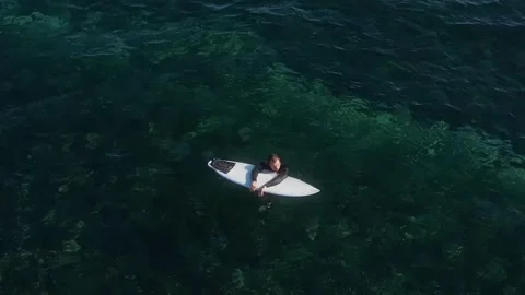 View from drone at man with his surfboard waits a wave in the sea Stock Footage 321049836
