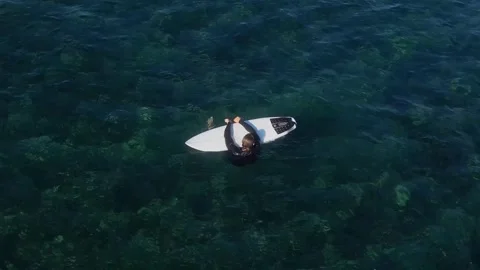 View from drone at man with his surfboard waits a wave in the sea Stock Footage 321049853