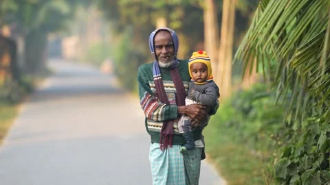 View of an elderly man holding a child on a rural road, Bangladesh. 動画素材 334957170