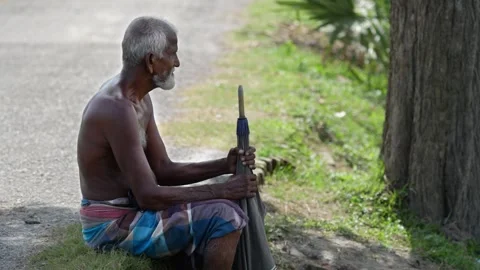 View of an elderly man sitting by a road with an umbrella, Bangladesh. 스톡 동영상 334958699