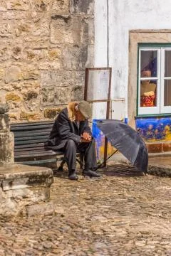 View of elderly with typical coat, sitting on wooden bench Stock Photos
