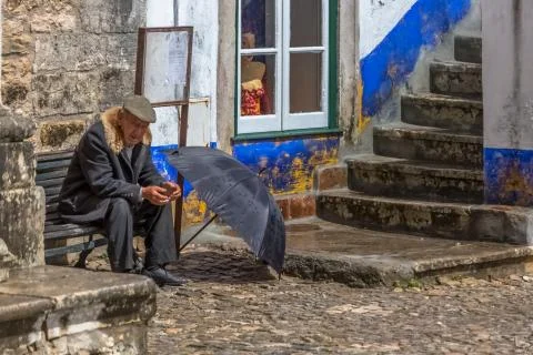 View of elderly with typical coat, sitting on wooden bench Stock Photos