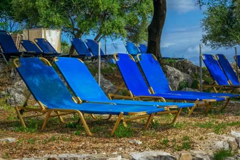 View of empty beach - blue deck chairs and umbrellas, cliffs and rocks Stock Photos