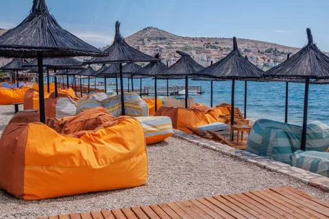 View of empty beach – bright orange bag chairs and straw shade umbrellas Stock Photos