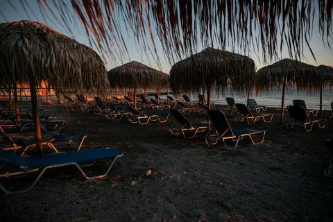 View of an empty rocky beach with sun loungers and parasols at sunrise. Stock Photos