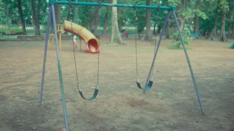 View of empty swings gently hanging in a quiet playground surrounded by trees. Stock Footage 341756357