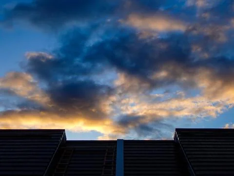 View of the evening sky with golden clouds over the roof silhouette Stock Photos