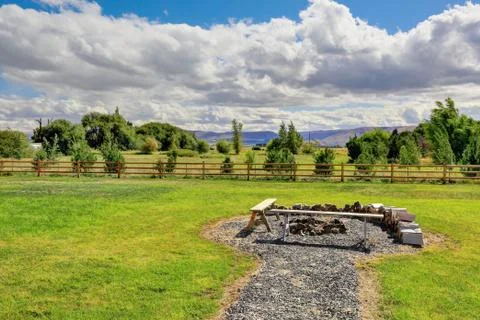 View of fire pit and firewood in spacious grass filled back yard. Stock Photos