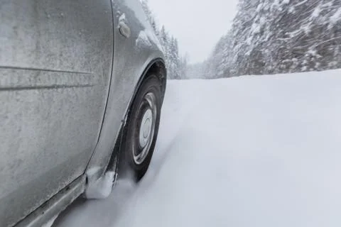 View focused on the car tire during in motion on snowy rural road during Stock Photos
