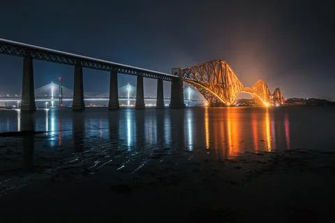 View of Forth Rail Bridge at night and and the glow trail of a moving train over Stock Photos