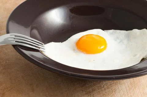 View of a fried egg served on dark dish with fork Stock-Fotos