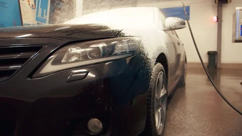 View of the front of a black car is being sprayed with white washing foam Stock Footage 316415520