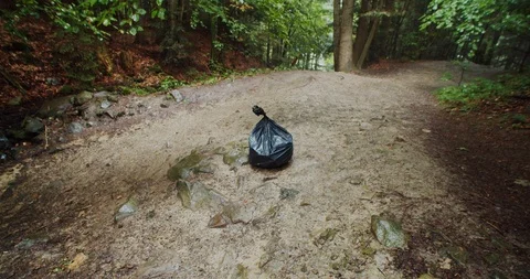 View of garbage bag with plastic trash lying on ground in clean green mountain Stock Footage 114580054