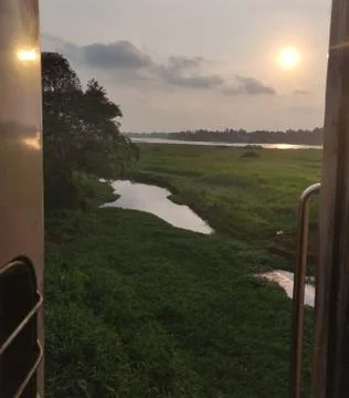A view of green fields and pond through an Indian Train door. Evening sunset. Stock Photos