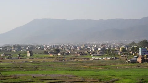 View of green fields and urban sprawl against hazy mountains, Nepal. Видео 335607482