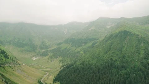 View of a green valley with a winding river, mountains, and cloudy sky in the ba Stock Footage 343843453