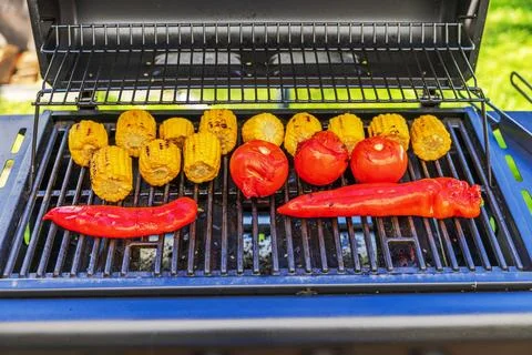 View of grilled corn cobs, roasted tomatoes and sweet red peppers cooking Stock Photos