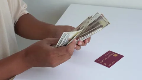 A view of a hand counting dollar bills with a credit card on a table. Stock Footage 338170074