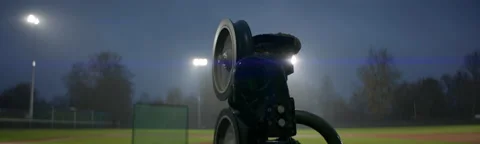 View of hand-fed pitching machine standing on a baseball field under heavy rain Stock Footage 221897518